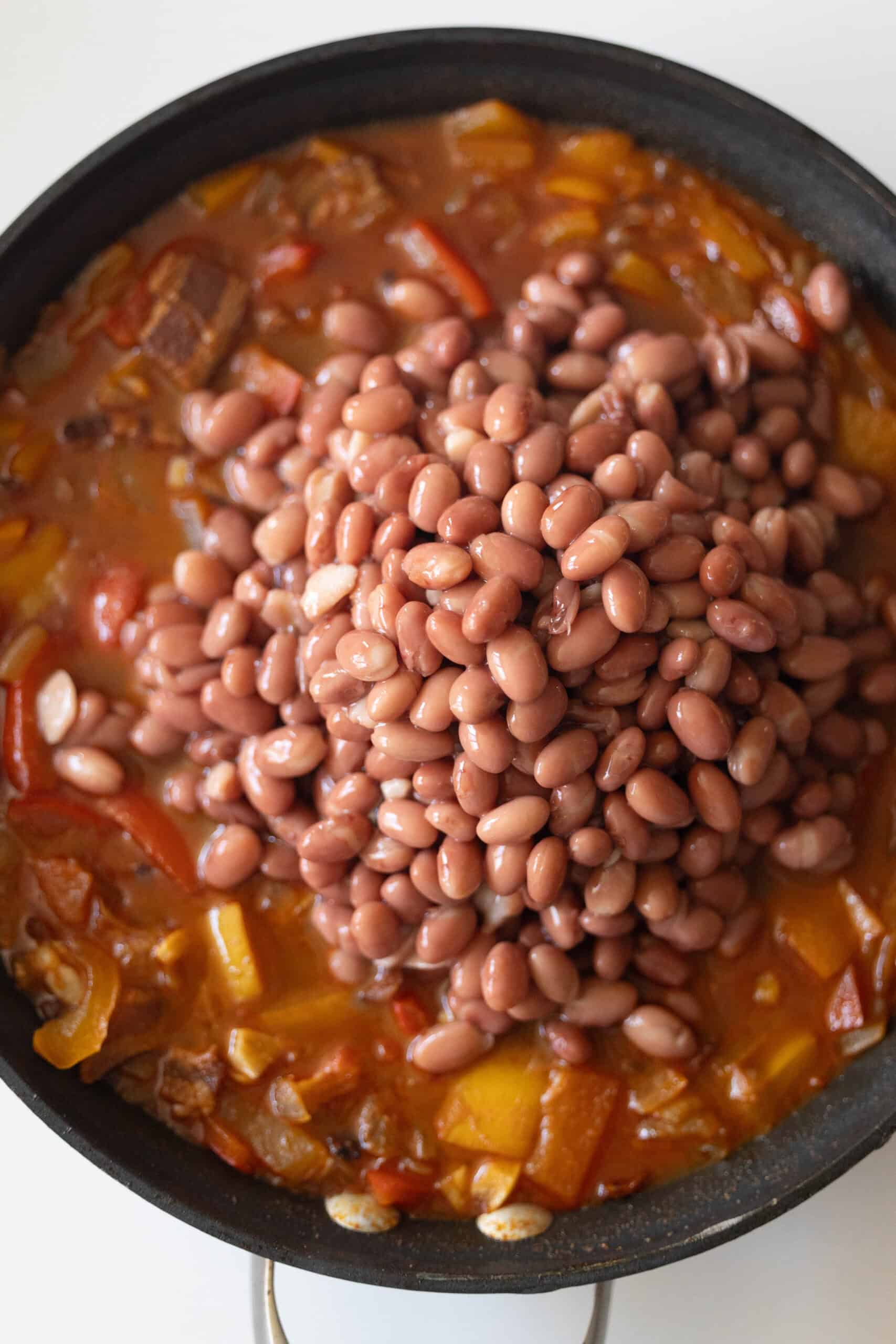 A skillet filled with a vegetable and tomato stew topped with a pile of Mexican beans, reminiscent of a traditional recipe.