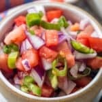 A bowl filled with chopped tomatoes, red onions, and green chili peppers, mixed together for a fresh salsa known as Pico de Gallo.