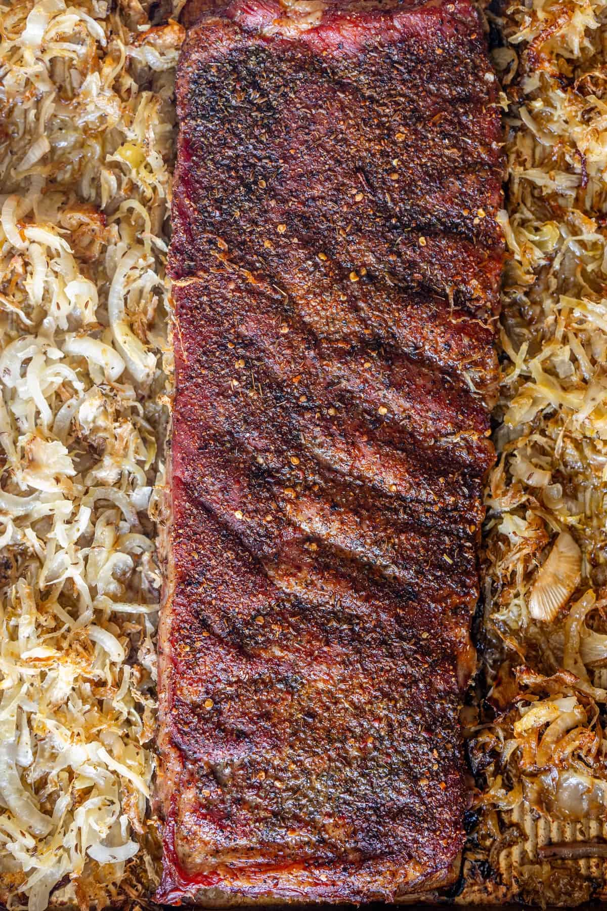 A seasoned rack of roasted ribs is surrounded by cooked sauerkraut and onions on a baking sheet, creating a flavorful roasted ribs recipe perfect for any comfort food lover.