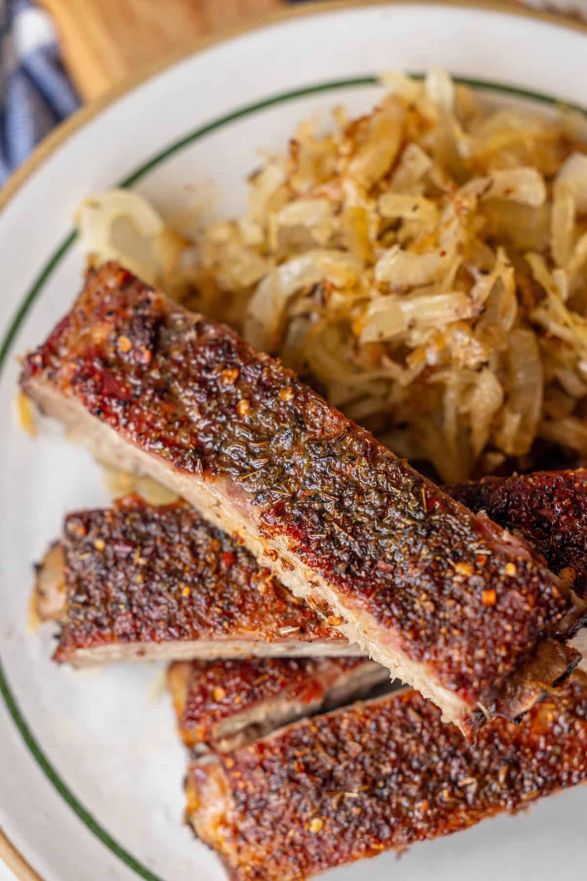 Three seasoned roasted ribs are stacked on a plate next to a serving of sautรฉed onions.