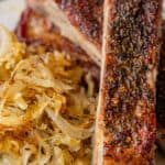 Close-up of seasoned, roasted ribs paired with a side of savory cooked cabbage and sauerkraut on a plate.