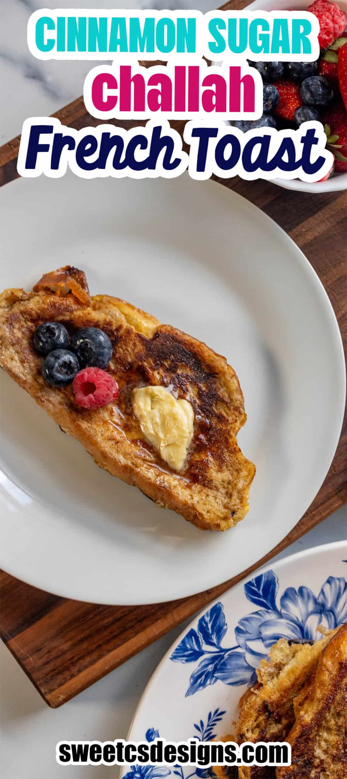 A slice of challah cinnamon sugar French toast with butter and berries on a white plate, next to a bowl of mixed berries.