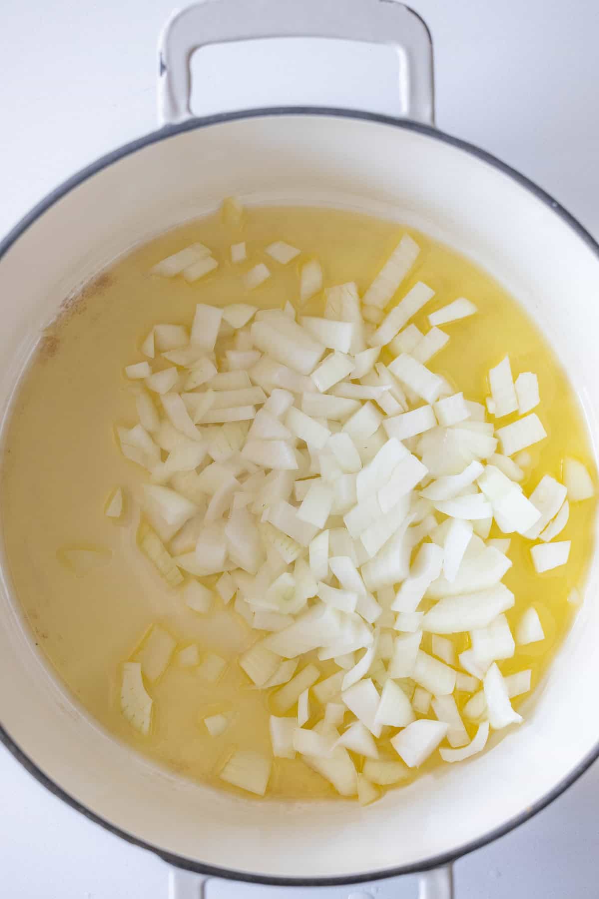 Chopped white onions in a large pot with oil, ready to be cooked for a flavorful pickle soup.