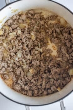Cooked ground meat and chopped onions in a white pot, with some browning on the bottom and sides of the pot, create a savory base perfect for starting a hearty sausage soup.