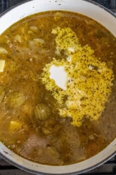 A pot of soup with visible onions, herbs, and a swirl of cream on the surface, simmering on a stovetop, features hearty slices of sausage adding richness to every spoonful.