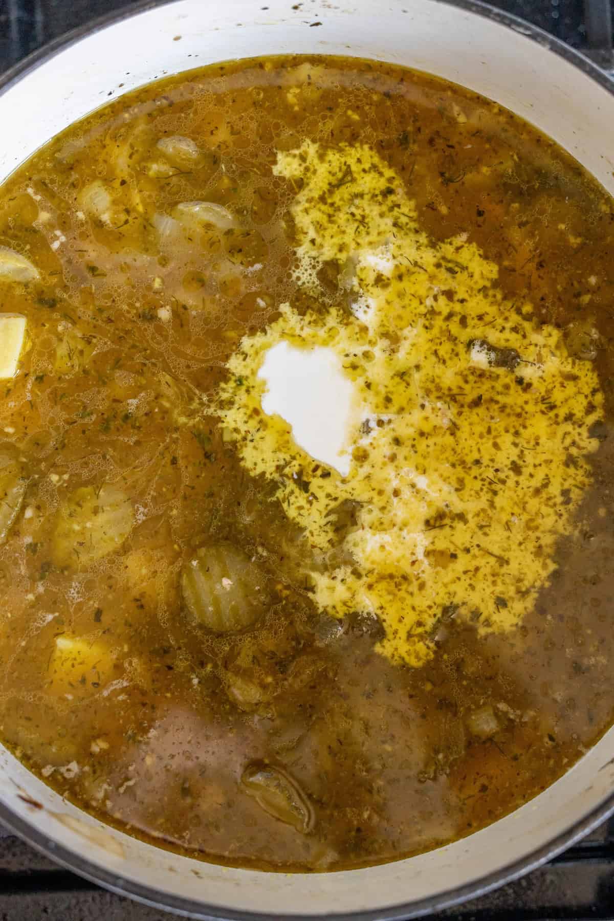 A pot of soup with visible onions, herbs, and a swirl of cream on the surface, simmering on a stovetop, features hearty slices of sausage adding richness to every spoonful.