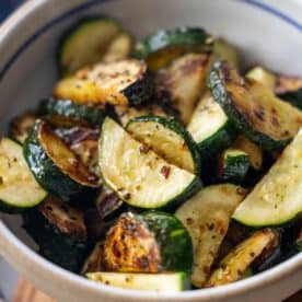 Bowl of roasted zucchini slices, inspired by classic zucchini recipes, seasoned with herbs and spices and showing a slightly charred and golden appearance.