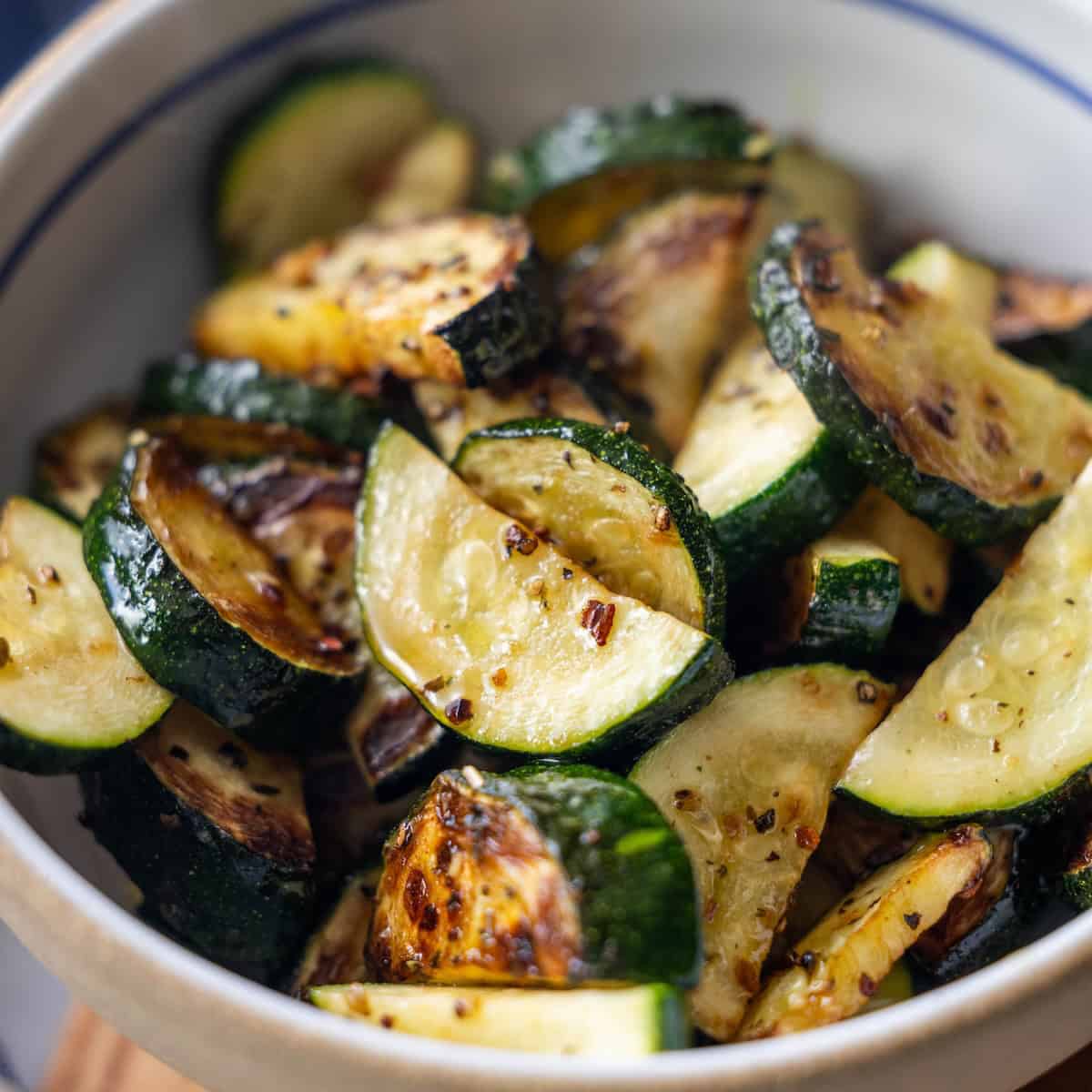 Bowl of roasted zucchini slices, inspired by classic zucchini recipes, seasoned with herbs and spices and showing a slightly charred and golden appearance.