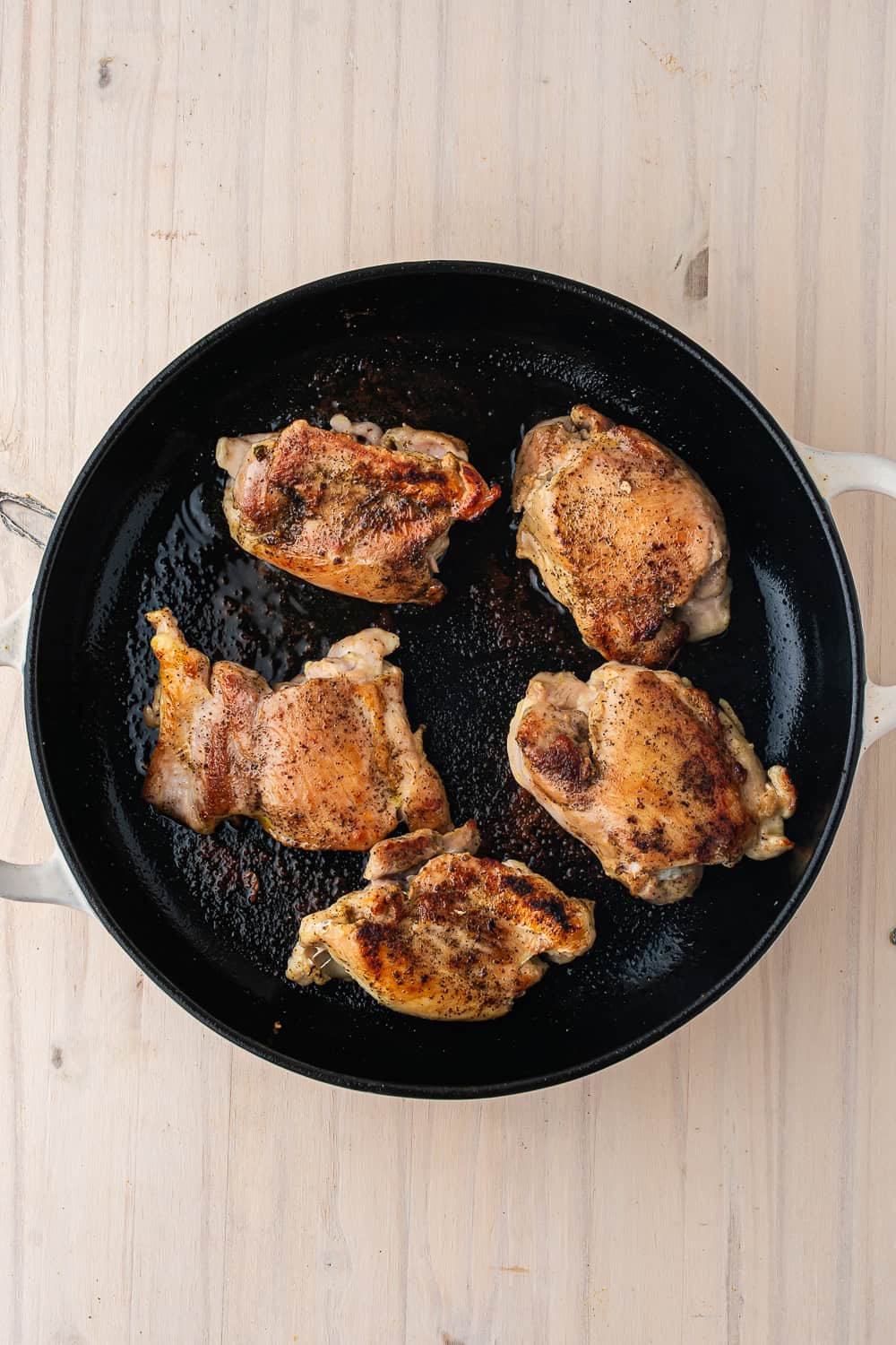 Five seasoned chicken thighs searing in a cast-iron skillet for a one pot chicken and rice dish.