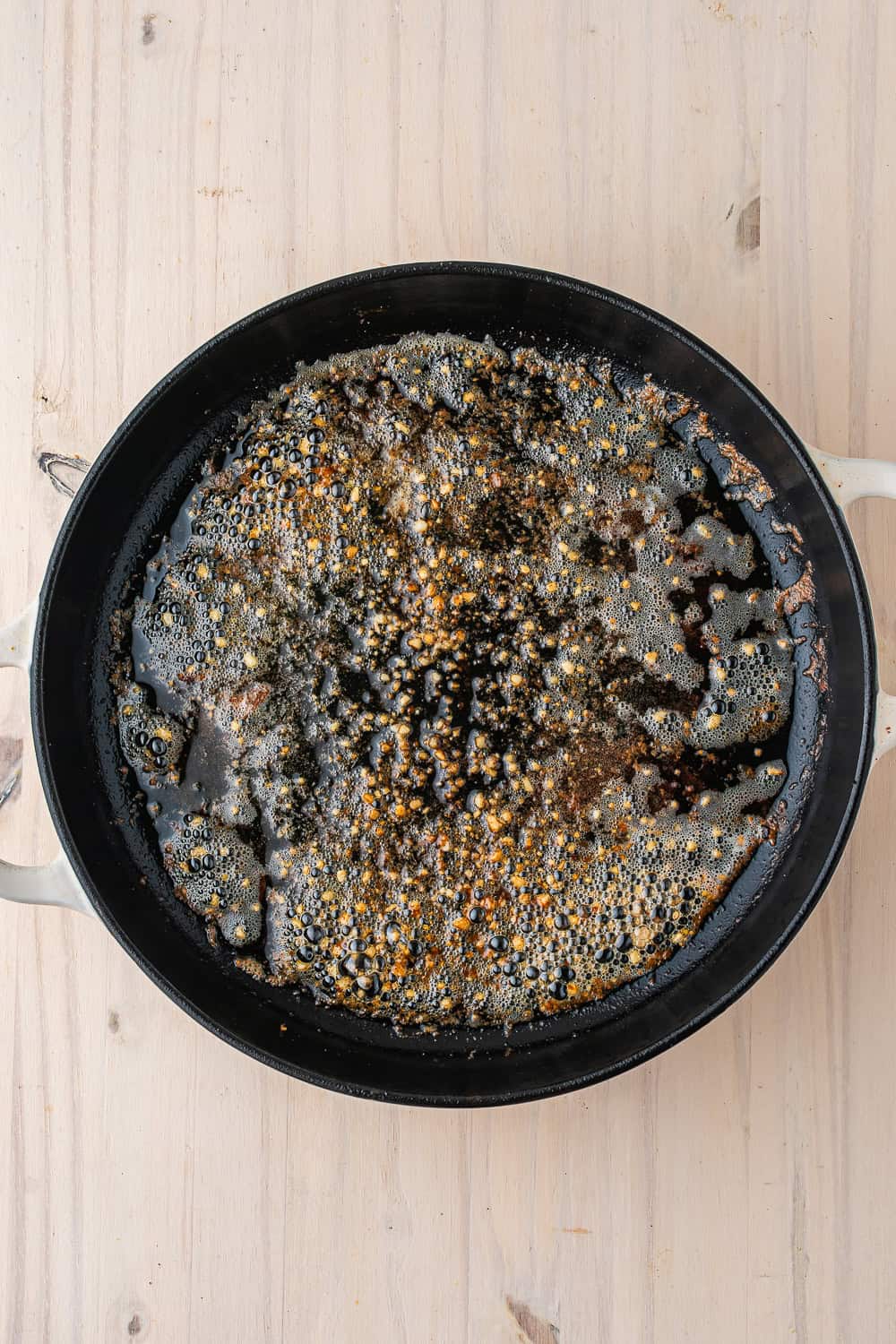A cast-iron skillet containing browned butter and minced garlic for a one-pot chicken and rice dish, set on a wooden surface.