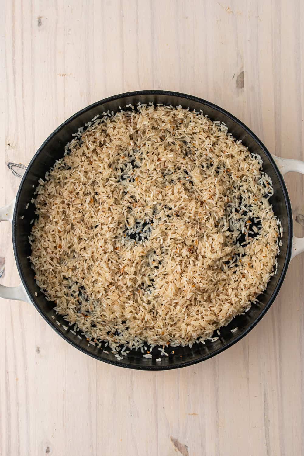 Lightly toasted white rice for a one-pot chicken meal in a cast-iron skillet.