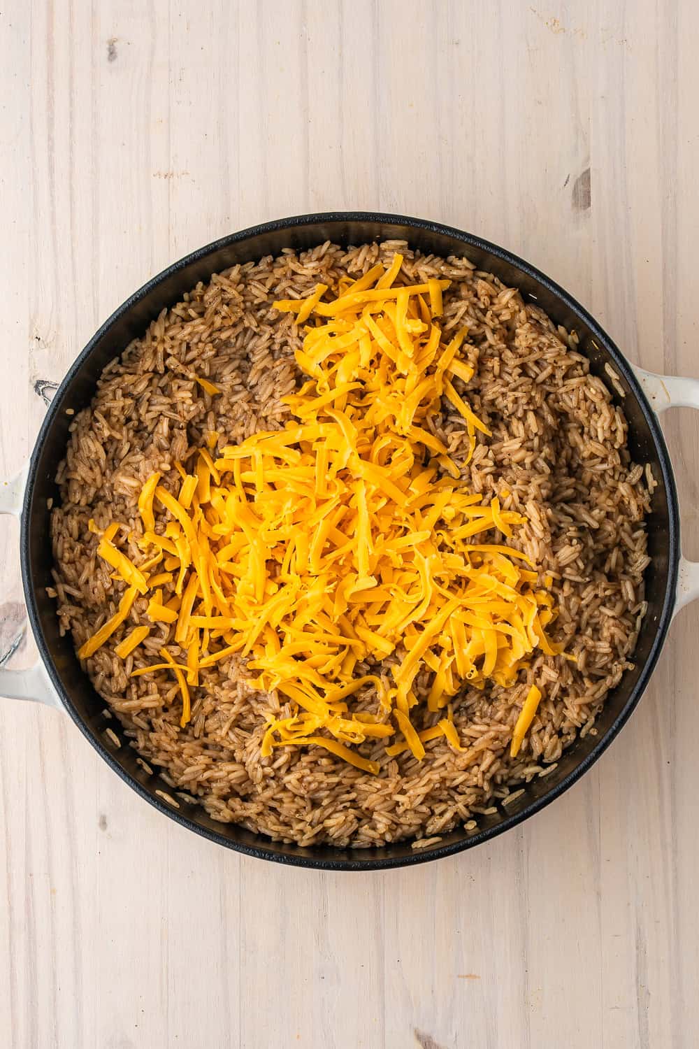 A skillet of cheesy chicken and rice topped with a mound of shredded cheddar cheese.