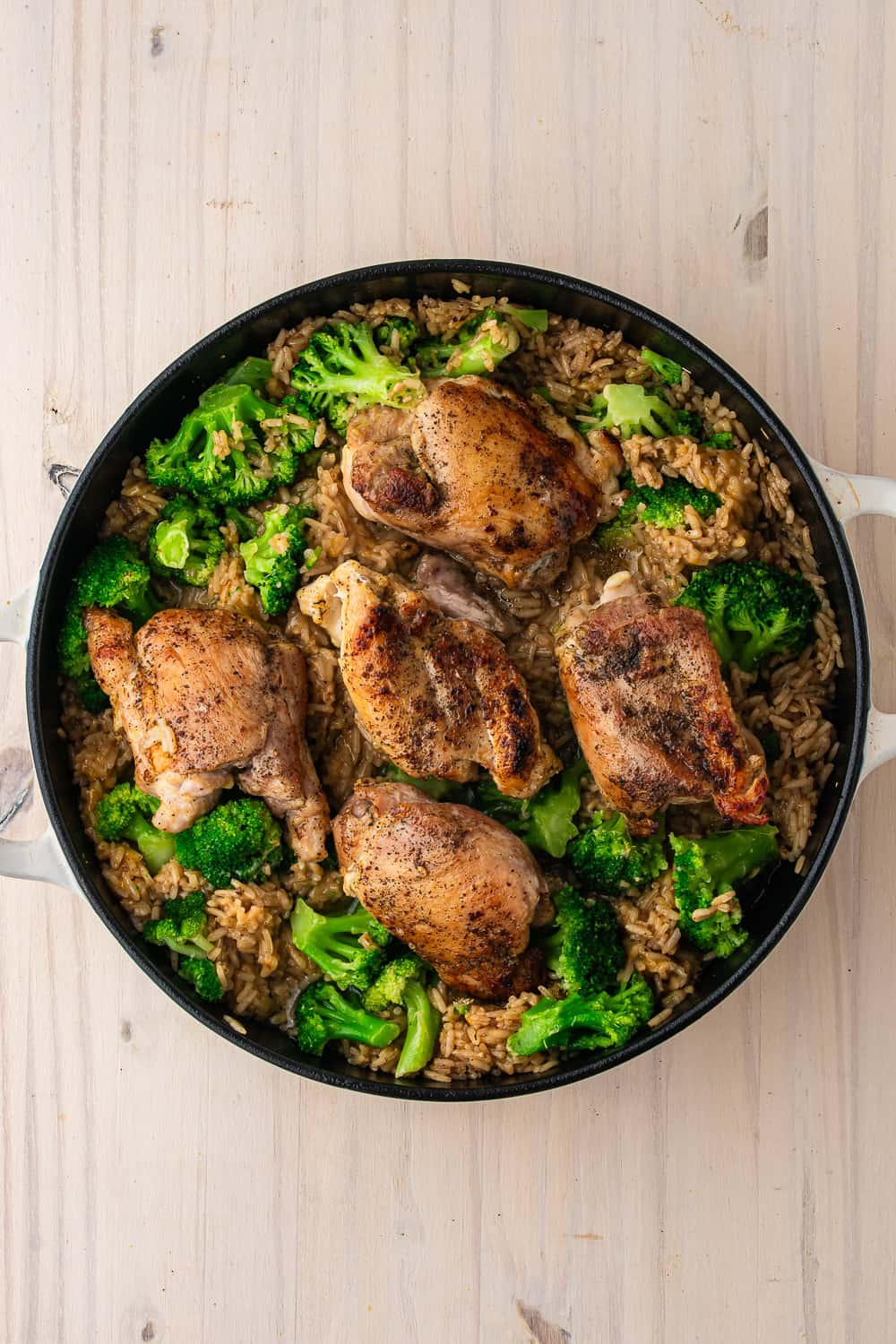 A skillet of one-pot chicken and rice with seasoned thighs and broccoli.