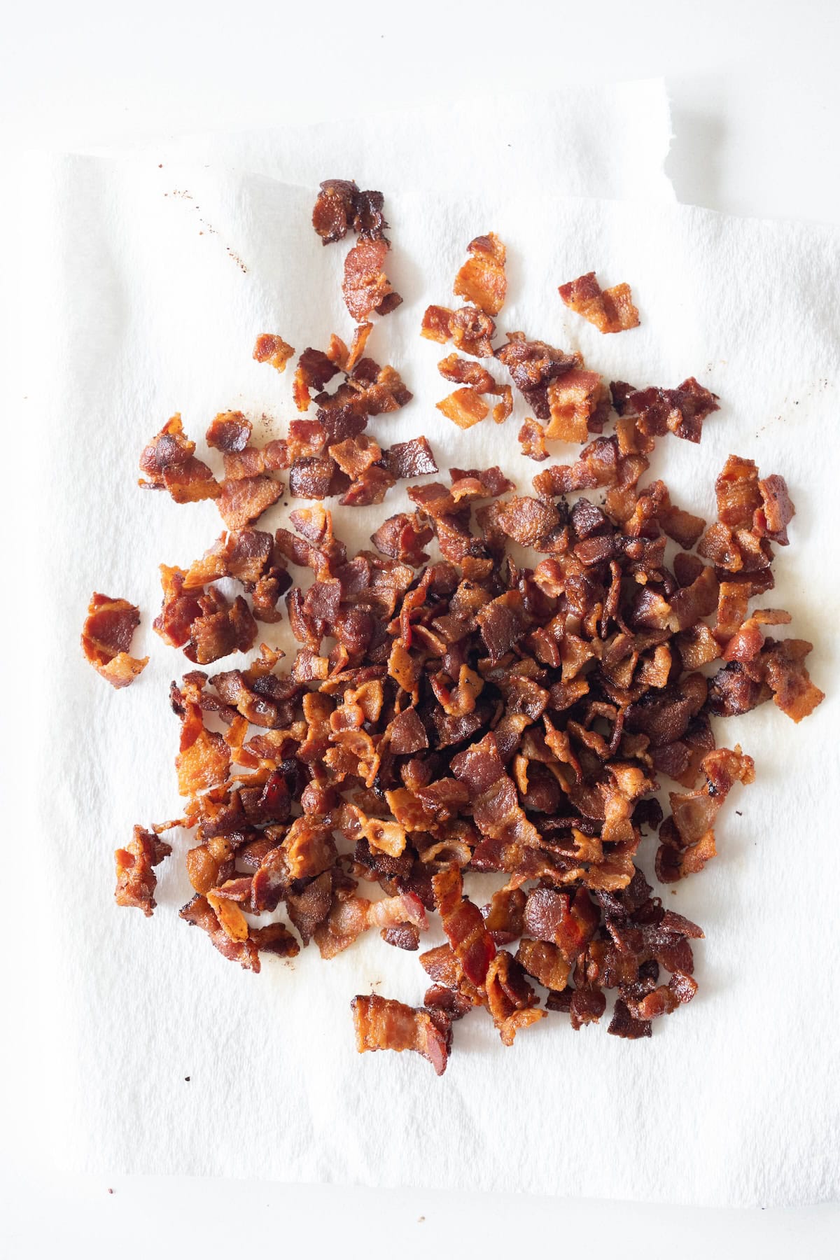 A pile of crispy bacon bits for a cheesy potato bake resting on a white paper towel.