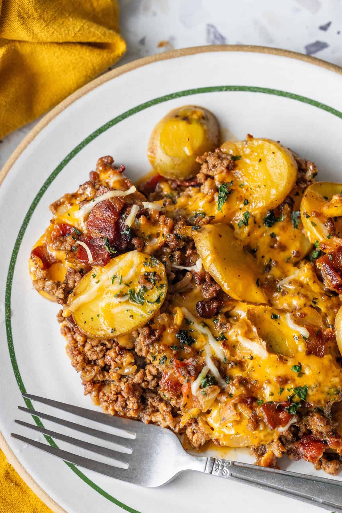 A plate of cheesy potato bake with ground beef, topped with melted cheese and bacon.