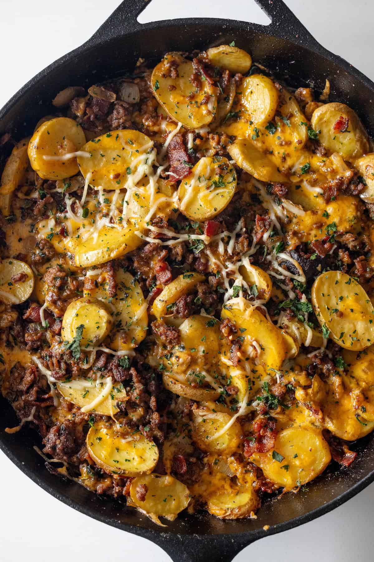 Skillet beef casserole of sliced potatoes, ground meat, and bacon topped with melted cheese and herbs.