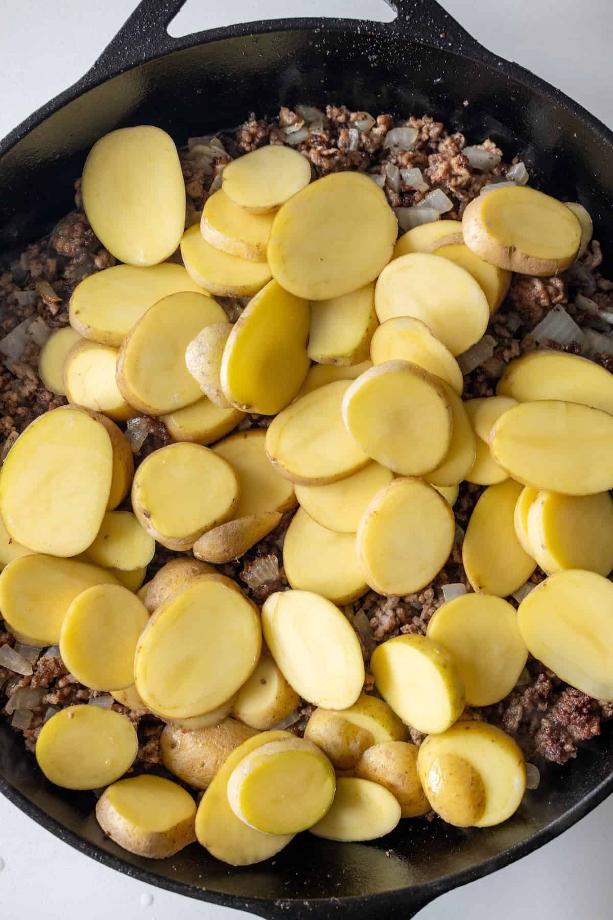 Sliced gold potatoes layered over ground meat and onions in a cheesy potato bake served in a cast-iron skillet.