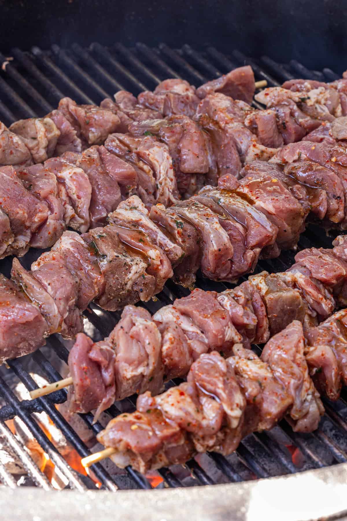 Skewers of onion-marinated pork cooking on a grill grate over hot coals.