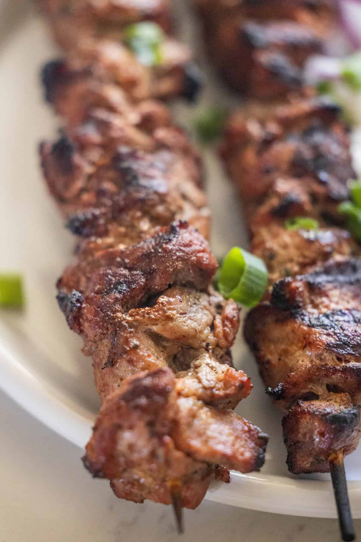 Two skewers of onion marinated pork garnished with sliced green onions on a white plate.