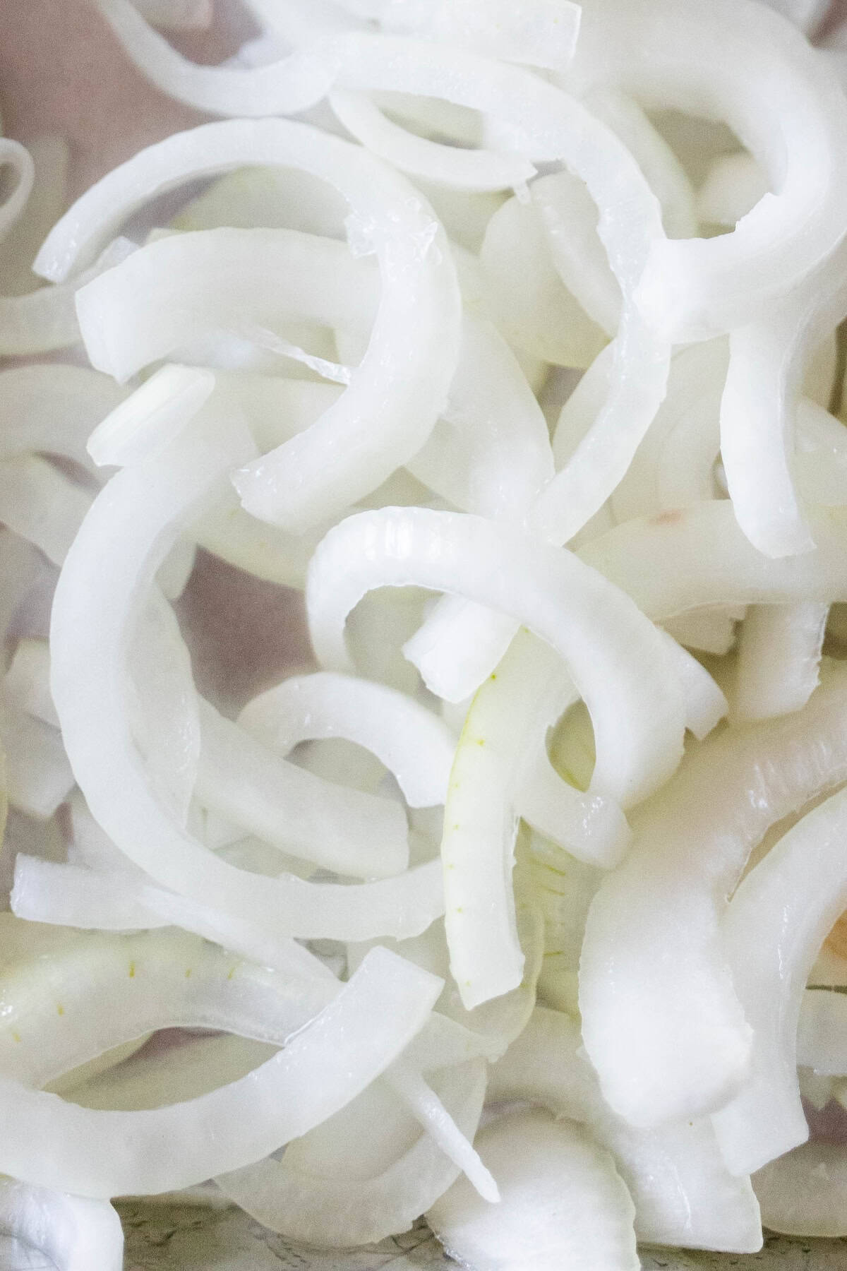 Thinly sliced raw white onion pieces for an onion marinated pork recipe.